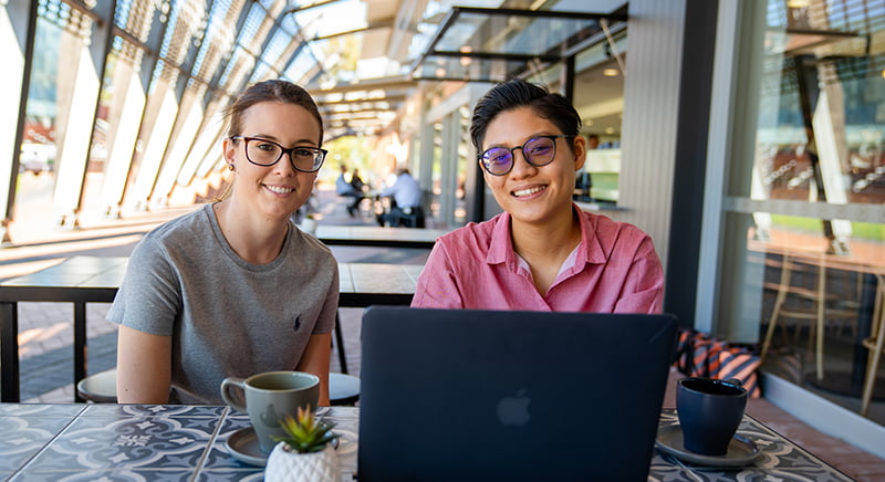 Two students sitting having coffee with a laptop.