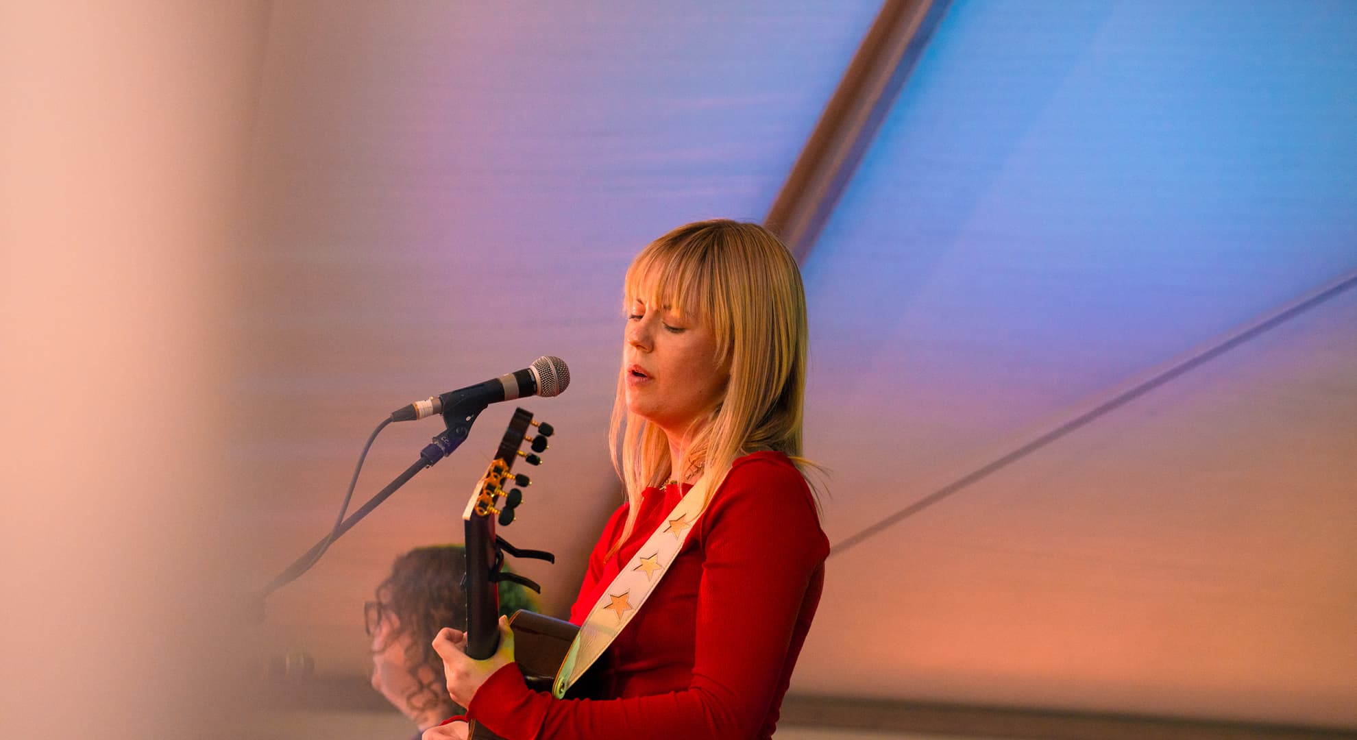 A side-on view of Clare on stage, playing guitar in front of a microphone